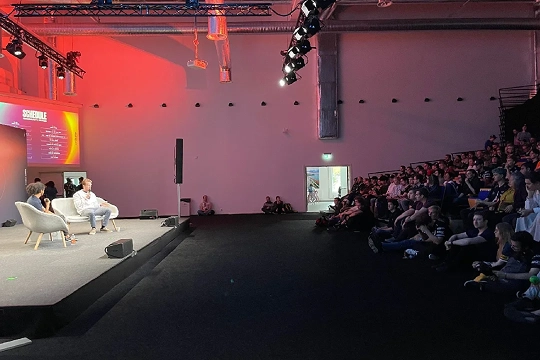 spreker op podium tijdens conferentie met publiek in zaal